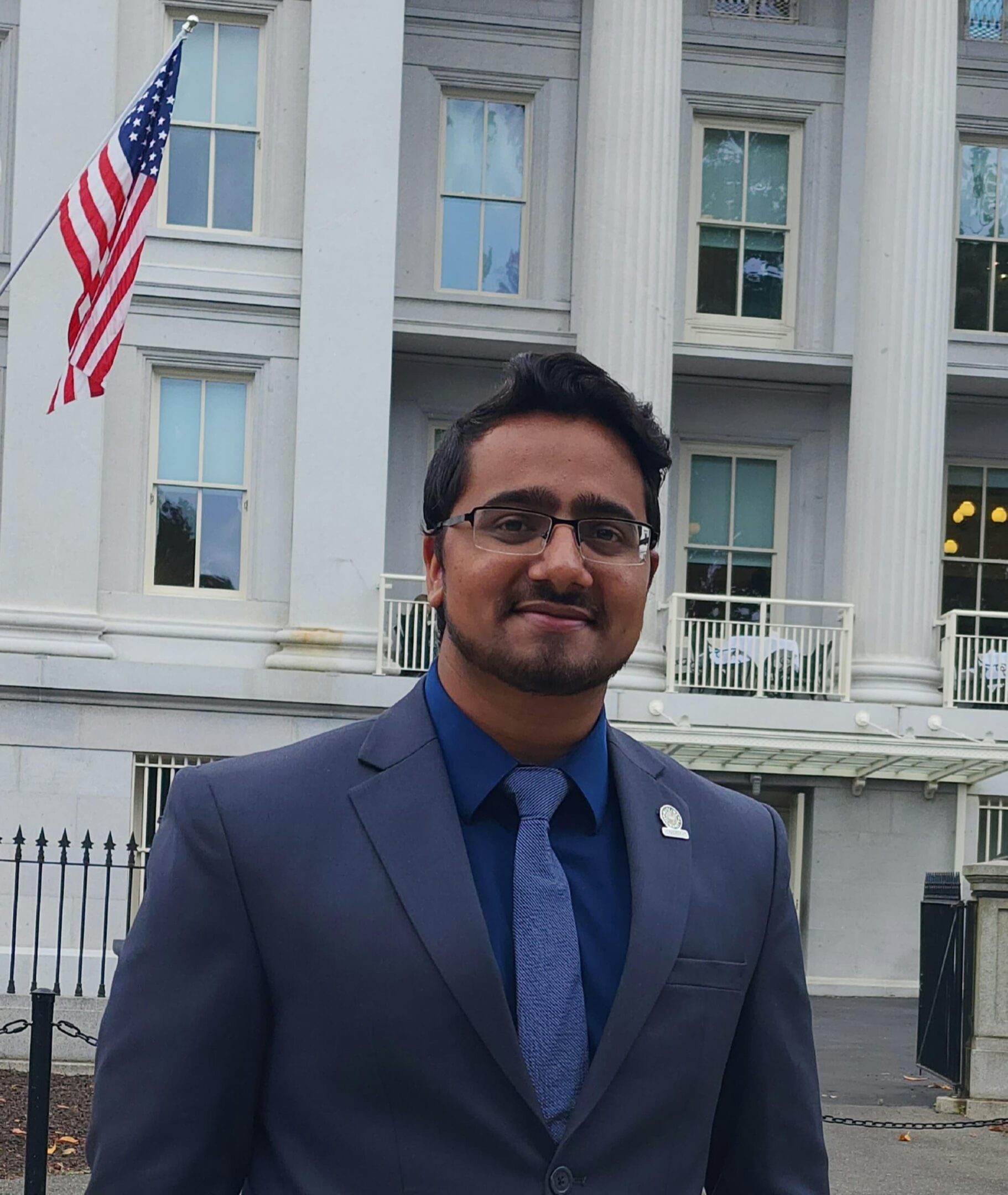 Man in suit and tie standing outside a building with American flags.