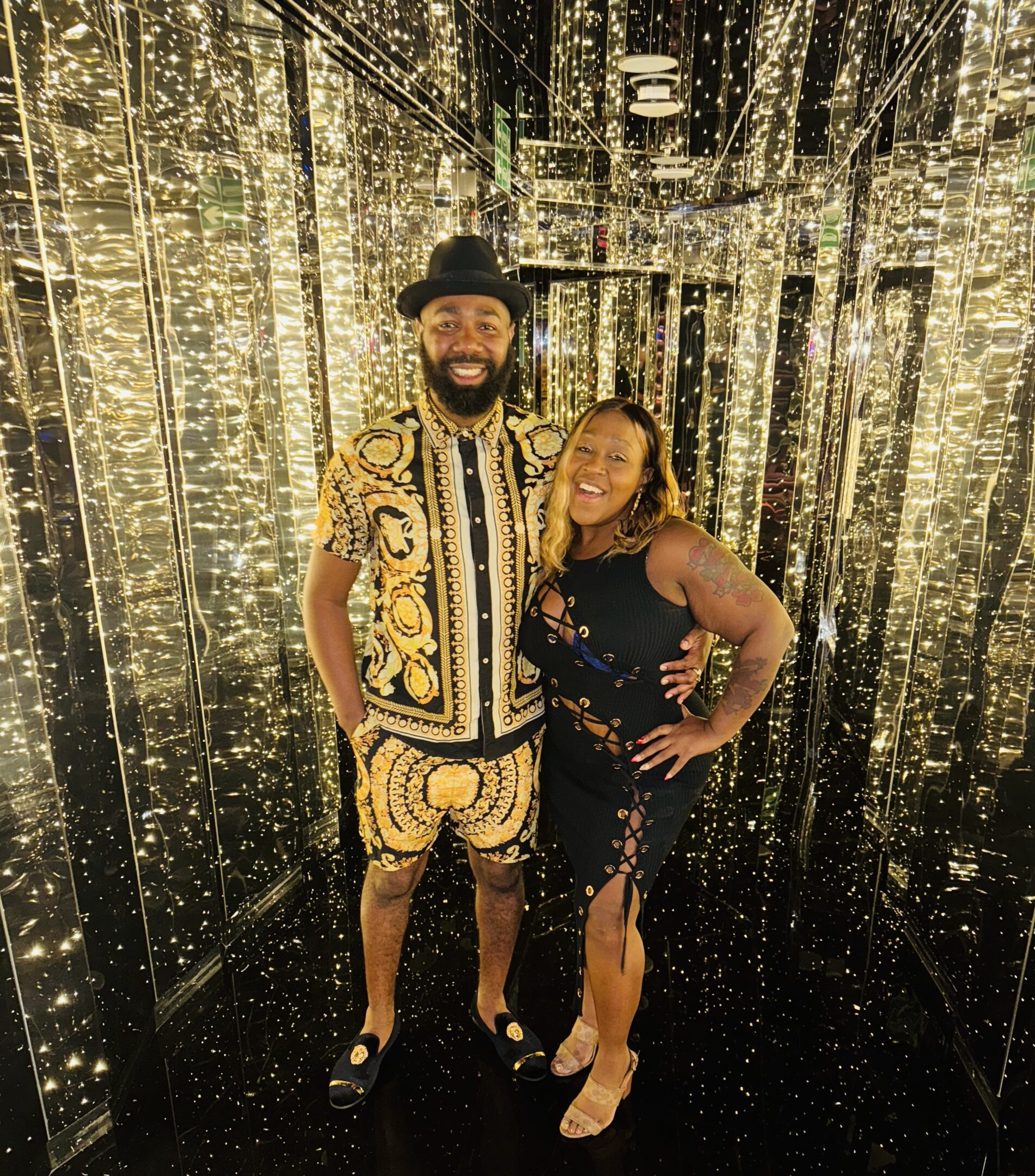 A stylish couple posing in front of a shimmering gold backdrop.