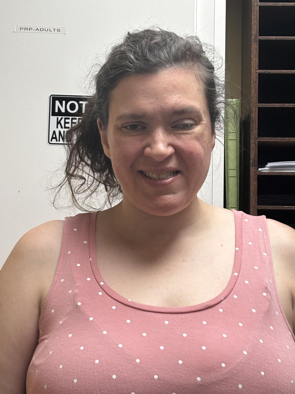 Smiling woman in a pink polka-dot tank top indoors.