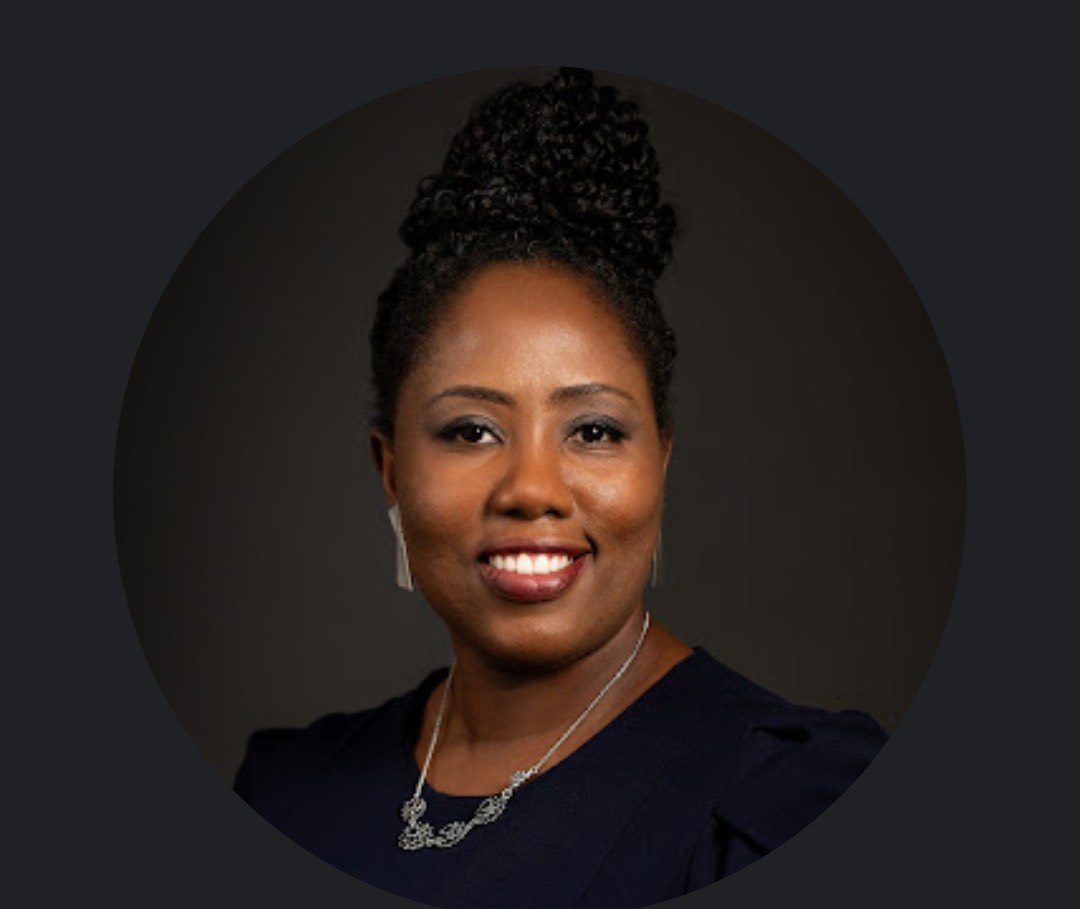 Professional portrait of a smiling woman with curly hair in a dark background.