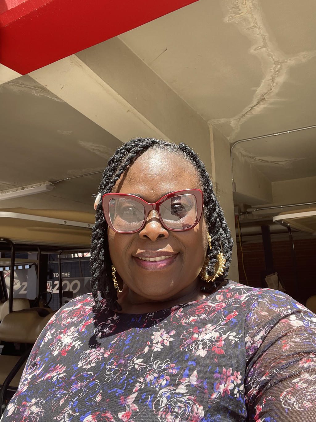 Smiling woman with glasses and braids outdoors in sunlight.